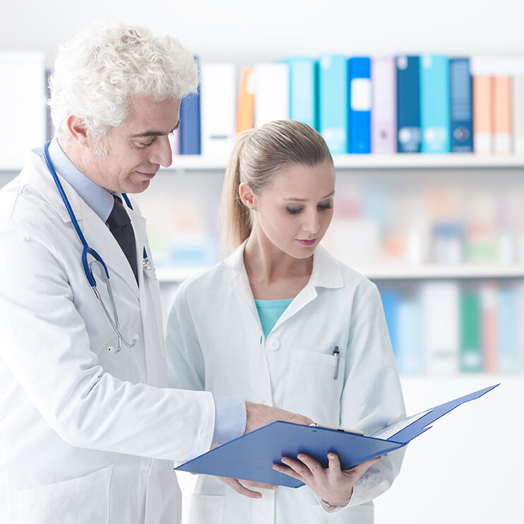 Confident doctor in the office checking medical records with his assistant, healthcare and teamwork concept